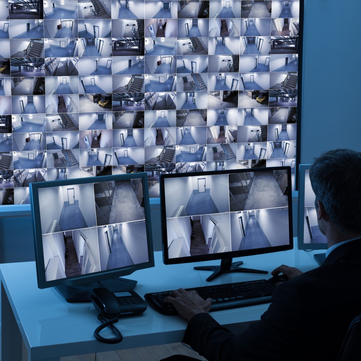 Rear View Of A Man In Control Room Monitoring Multiple Cctv Footage