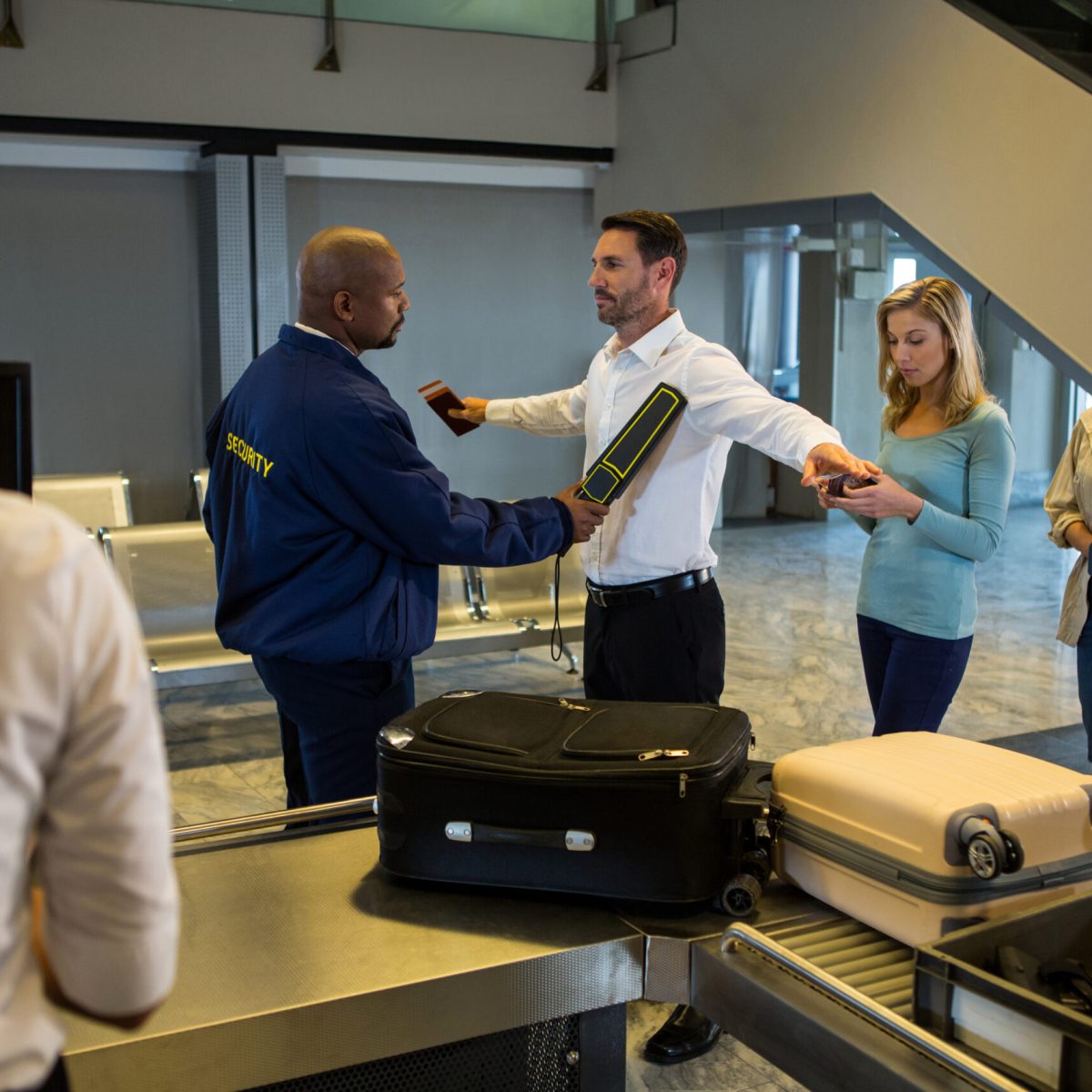 Security guard frisks passengers standing in queue at airport terminal